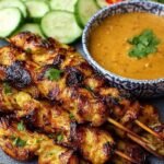 Grilled chicken skewers with a side of creamy peanut dipping sauce and lime wedges.