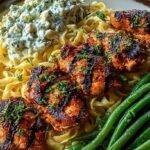 A plate of creamy fettuccine alfredo topped with smoky chicken strips, charred green beans, and a dollop of white feta cream.