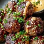 A platter of glazed Korean BBQ meatballs with sesame seeds and a side of spicy mayo dip.