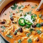 A bowl of creamy orange chicken enchilada soup topped with shredded cheese and black beans.
