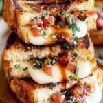 A golden brown sourdough grilled cheese sandwich pulled apart to show melted mozzarella and fresh tomato bruschetta filling.