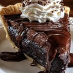 A slice of warm hot fudge pie served with a scoop of melting vanilla ice cream on a white plate.