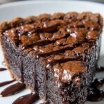 A slice of gooey brownie pie with a crackly top and melted chocolate chips inside a buttery crust.