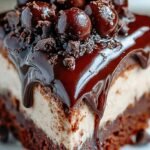 A close-up shot of layered no-bake cheesecake brownies with chocolate ganache and brownie chunks on top.