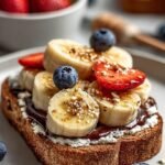 Two slices of whole grain toast topped with cottage cheese, sliced bananas, chocolate shavings, and a drizzle of honey.