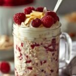 A glass jar filled with creamy raspberry overnight oats topped with fresh berries and chia seeds.