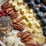 A thick yellow smoothie bowl topped with granola and fresh berries in a white ceramic bowl.