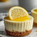 Six individual lemon cheesecake cups with a graham cracker crust in a muffin tin.