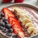 A thick pink strawberry smoothie bowl topped with granola, fresh strawberry slices, and chia seeds.