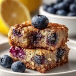 A stack of rectangular protein blueberry lemon snack bars showing oats and dried blueberries on a wooden board.