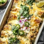 A 9x13 baking dish filled with cheesy green chicken enchiladas topped with sour cream, onions, and fresh cilantro.