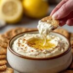 A bowl of creamy lemon cheesecake dip topped with graham cracker crumbs and served with fresh fruit.