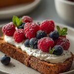 Two slices of golden toast topped with smooth whipped cottage cheese, fresh blueberries, raspberries, and lemon zest.