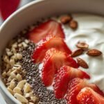 A creamy strawberry yogurt chia bowl topped with fresh sliced strawberries and crunchy almonds in a white ceramic bowl.