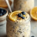 A glass jar filled with creamy lemon poppyseed overnight oats topped with fresh lemon zest and a sprig of mint.