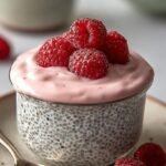 A glass jar filled with pink raspberry chia pudding topped with fresh berries and a dollop of yogurt.