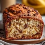 A golden brown loaf of cottage cheese banana bread sliced on a wooden board