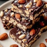 Homemade nut bars with dark chocolate drizzle and flaky sea salt on parchment paper