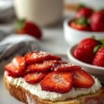 A slice of golden sourdough toast topped with creamy cottage cheese, sliced strawberries, honey, and fresh mint.