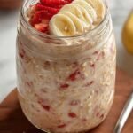 A glass jar filled with creamy strawberry banana overnight oats topped with fresh fruit
