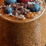 A glass jar filled with creamy chocolate chia seed pudding topped with fresh raspberries and a sprig of mint.