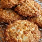 Golden brown breakfast cookies on a parchment-lined baking sheet with a drizzle of maple syrup