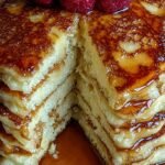 A stack of golden brown Greek yogurt protein pancakes topped with fresh berries and syrup