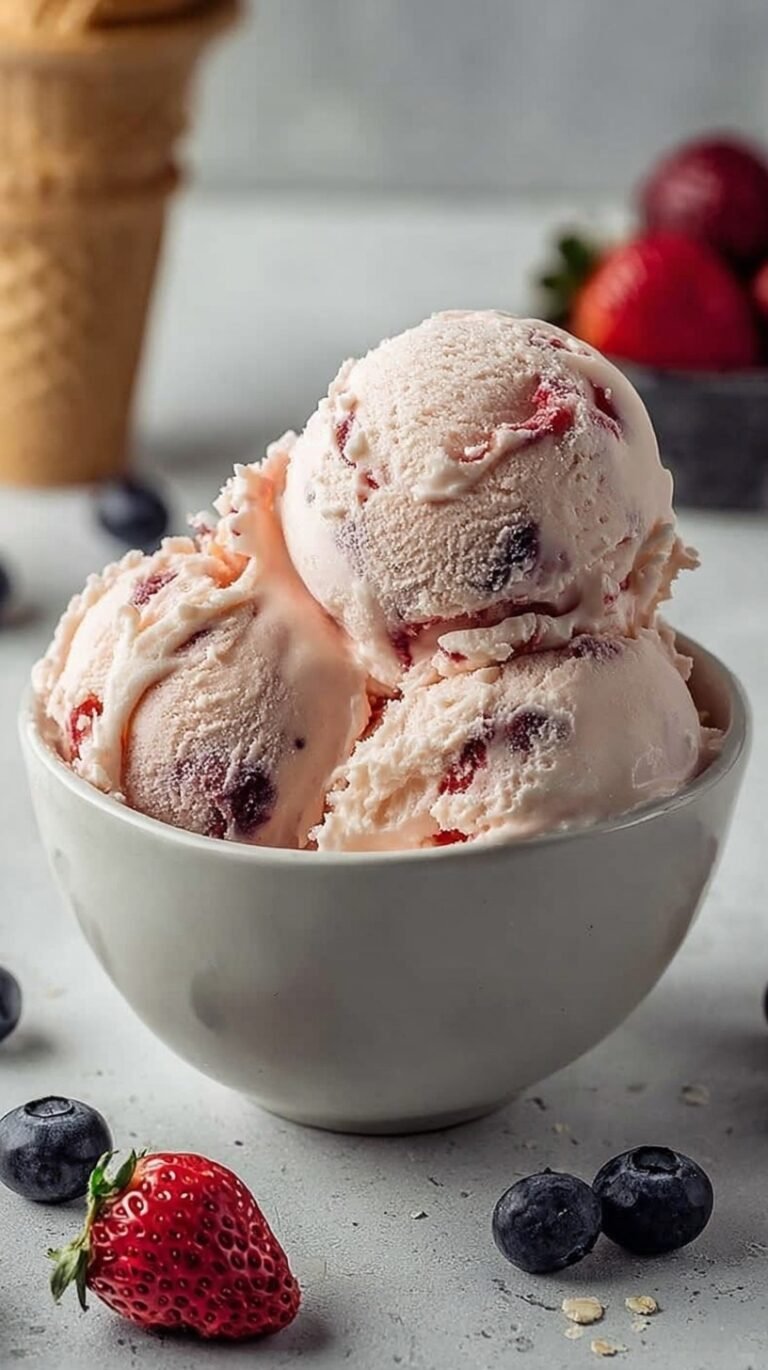 A scoop of creamy vanilla ice cream with swirls of red and blue berries in a white bowl.