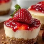Individual glass cups filled with layers of graham cracker crust, creamy cheesecake filling, and fresh diced strawberries on top.