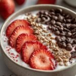 A fresh strawberry chia yogurt bowl with sliced berries, chia seeds, and granola on top of creamy Greek yogurt.