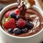 A bowl of smooth chocolate cottage cheese dip topped with fresh raspberries and chocolate chips.