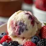 A scoop of creamy vanilla ice cream with fresh berries in a white bowl.