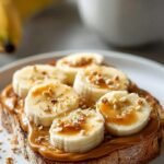 A slice of thick-cut whole grain toast topped with creamy peanut butter, white cottage cheese, sliced bananas, and a drizzle of honey.
