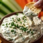 A bowl of smooth blended cottage cheese ranch dip surrounded by fresh vegetable sticks.