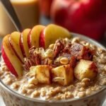 A glass jar filled with creamy overnight oats, diced apples, and chai spices on a wooden table.