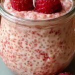 A glass jar filled with pink raspberry chia pudding topped with fresh berries