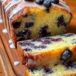 A golden loaf of freshly baked blueberry bread sliced on a wooden board.