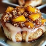 A tray of golden peach cobbler cinnamon rolls with vanilla glaze and streusel topping.