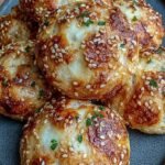 Golden brown mini pizza bagel bites topped with melted cheese and turkey pepperoni on a baking sheet.