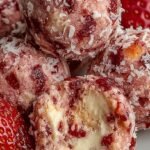 A plate of pink strawberry cheesecake protein balls dusted with crushed graham crackers and strawberry powder.