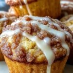 Golden brown cinnamon roll protein muffins with a white glaze drizzle on a cooling rack.