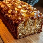 A golden brown apple cinnamon breakfast loaf sliced on a wooden board with fresh apples nearby.