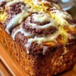 A golden loaf of High-Protein Cinnamon Roll Bread sliced on a wooden board showing cinnamon swirls.