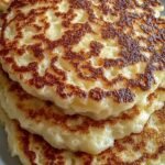 A stack of golden brown cottage cheese pancakes topped with fresh berries and a drizzle of syrup.