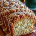 A golden loaf of eggnog bread topped with a thick layer of spiced crumb streusel on a wire rack.