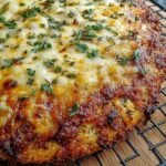 A golden brown cottage cheese pizza crust topped with melted cheese and fresh basil on a baking sheet.