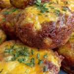 Golden brown hash brown sausage bites in a mini muffin tin with melted cheese and savory sausage crumbles.