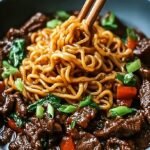 A steaming bowl of hoisin beef noodles with tender steak, broccoli, and red peppers