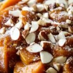 A ceramic baking dish filled with sliced sweet potatoes and apples in a honey glaze topped with pecans.