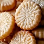 A stack of golden French butter cookies on a parchment-lined baking sheet